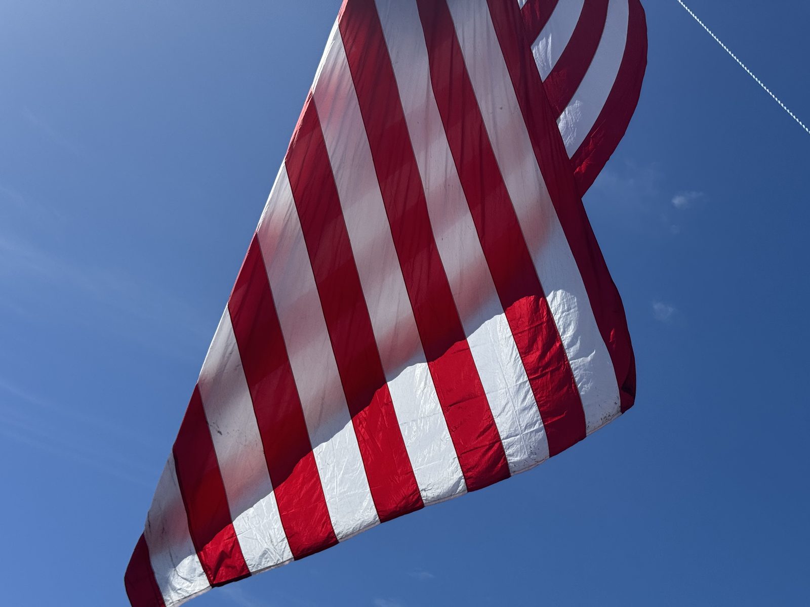 An enormous American flag hung from the boom of a crane, backlit against a deep blue sky