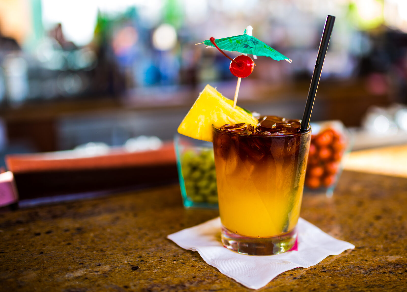 A layered Mai Tai on a bar in Honolulu — dark rum floating over a golden base, garnished with a pineapple wedge, a cherry, and a green paper umbrella