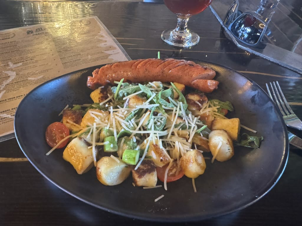 A plate of seared sausage over potato gnocchi, parmesan, with a snifter of dark beer in the background