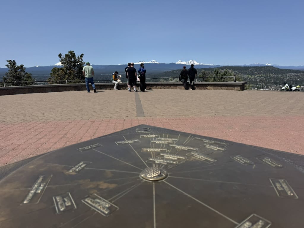 Bronze peak-finder plaque on the Pilot Butte summit pointing at the visible Cascade peaks, with the actual range in the background