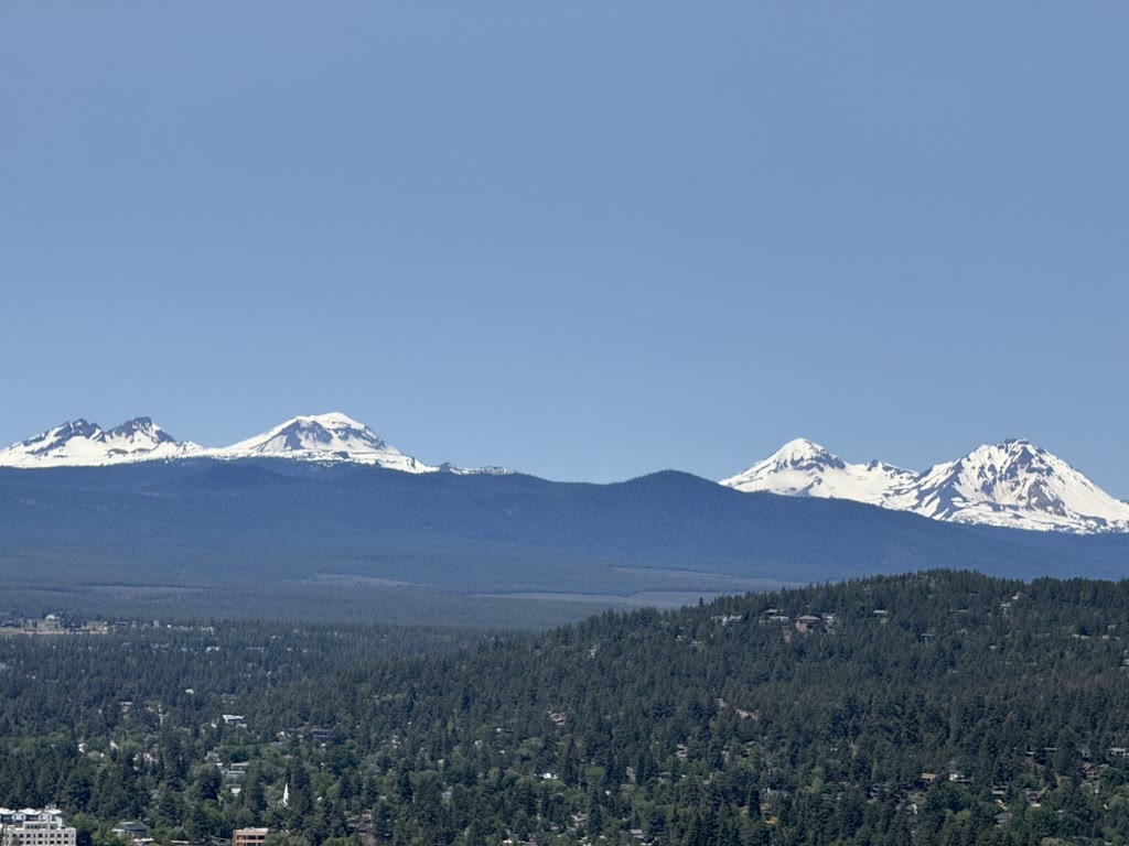 Three Sisters and Broken Top floating over a sea of pines
