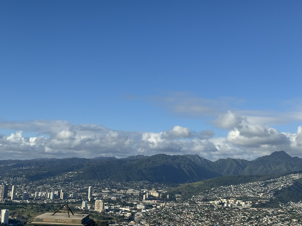 View into the Diamond Head crater from the rim trail — pale grass and scrub on the crater floor, ocean and Koko Head visible in the distance