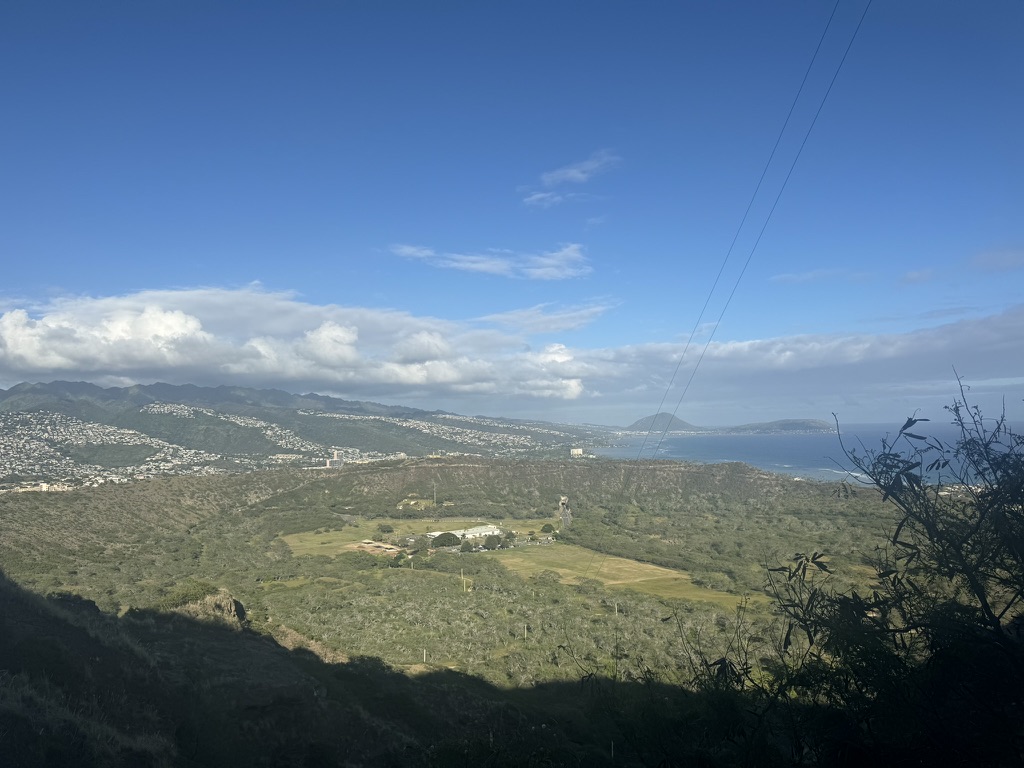 Looking out from Diamond Head's rim toward Koko Head — the green crater floor in the foreground, the blue Pacific stretching off the right edge of the island