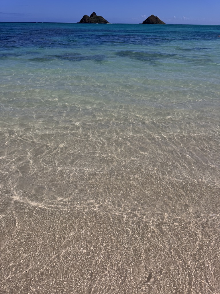 The Mokulua Islands seen across glass-clear shallow Lanikai water