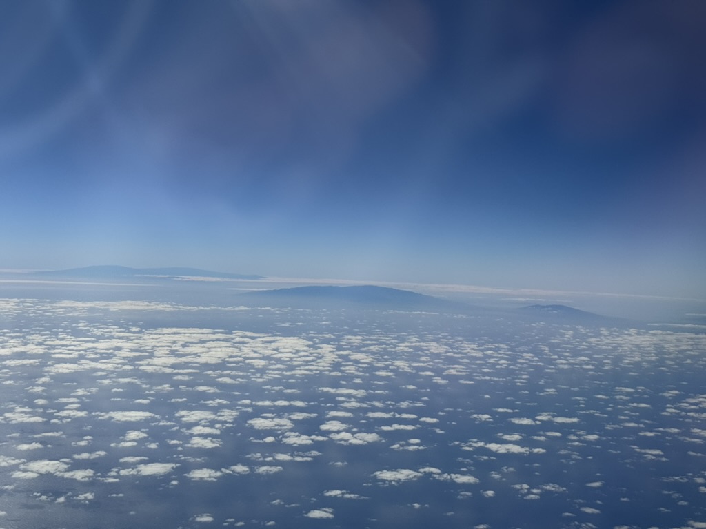 Wider view of the same volcanic silhouettes through a soft band of upper-altitude haze