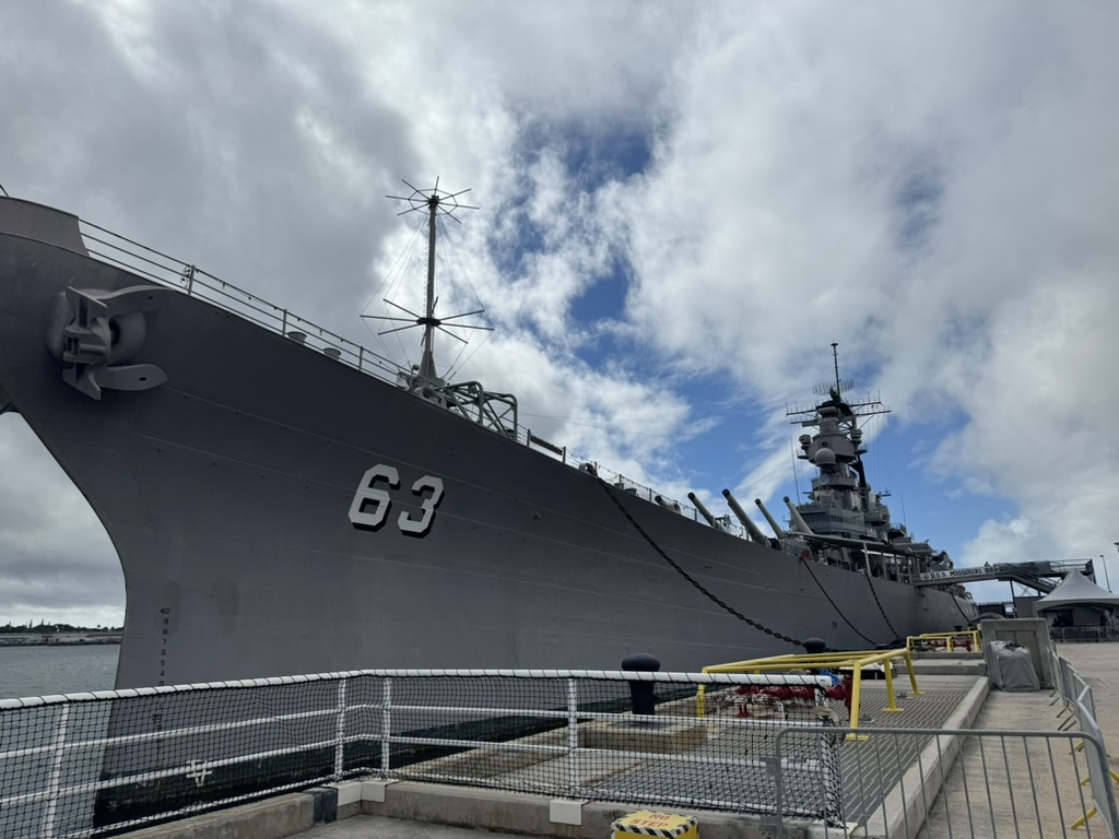 The forward Missouri deck under heavy cloud — American flags lining the gangway, tourists walking the access ramp toward the ship