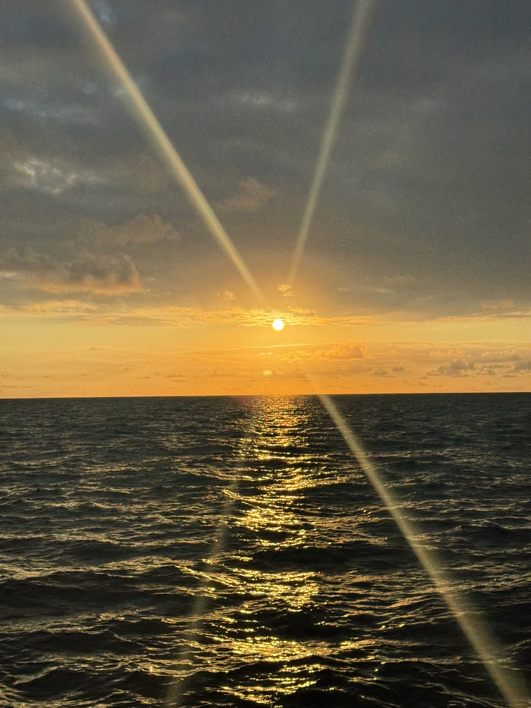 Sun setting through diffuse cloud, lens flare over open water