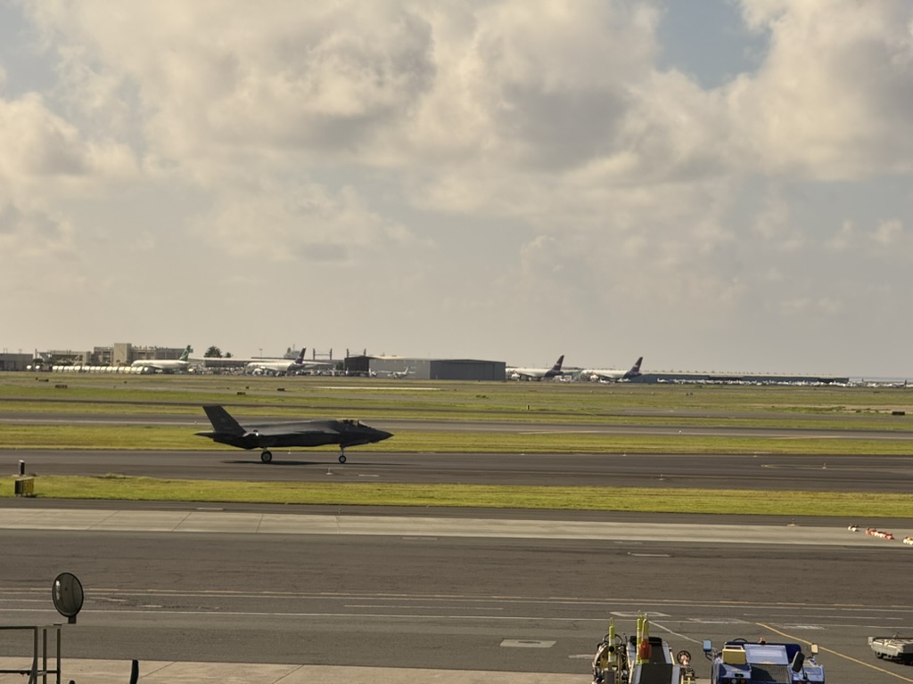 An F-35 Lightning II on the runway with commercial widebodies behind