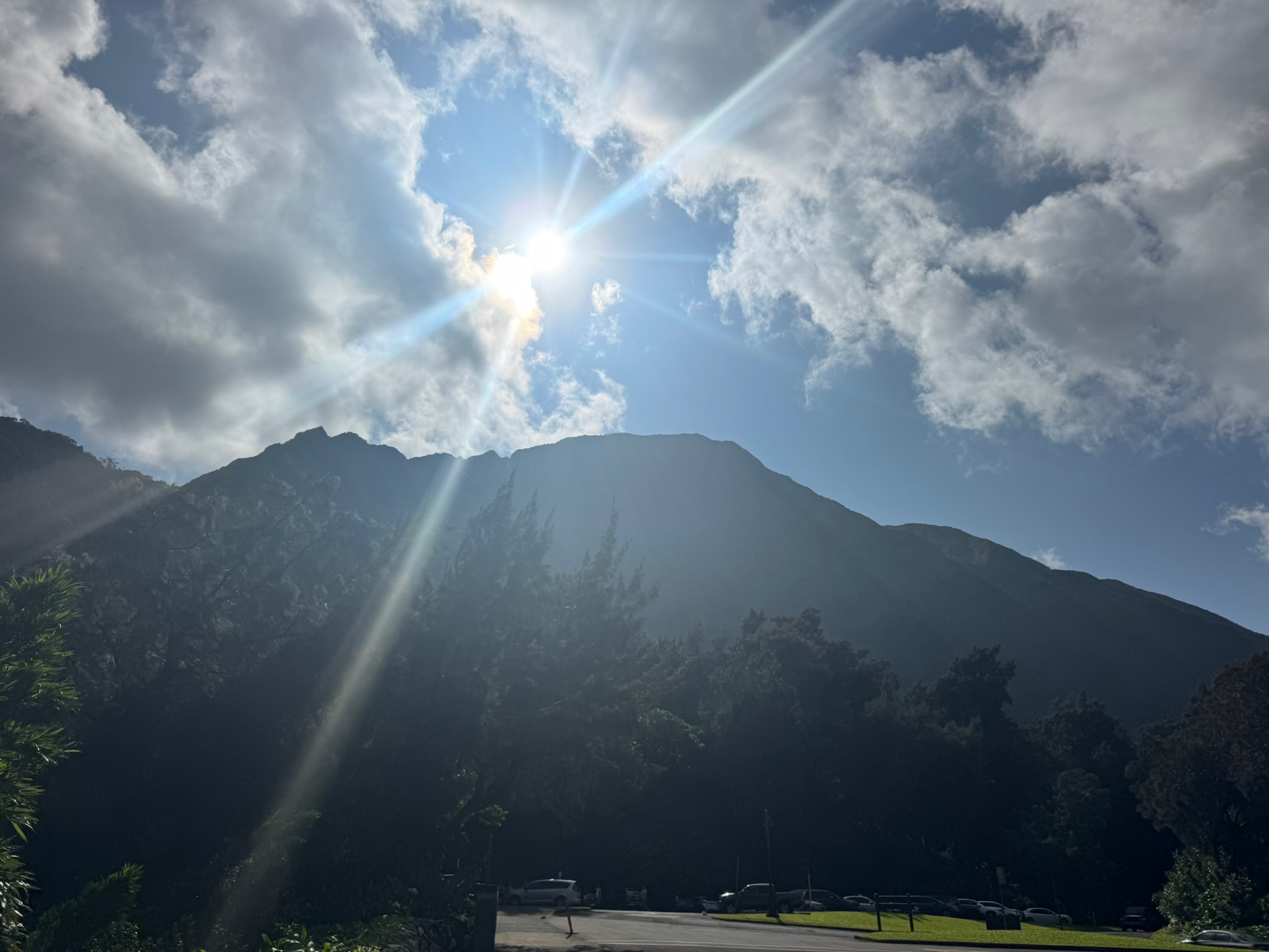 Sun cresting the Koʻolau ridge, rays splaying through the cloud cover above the trees