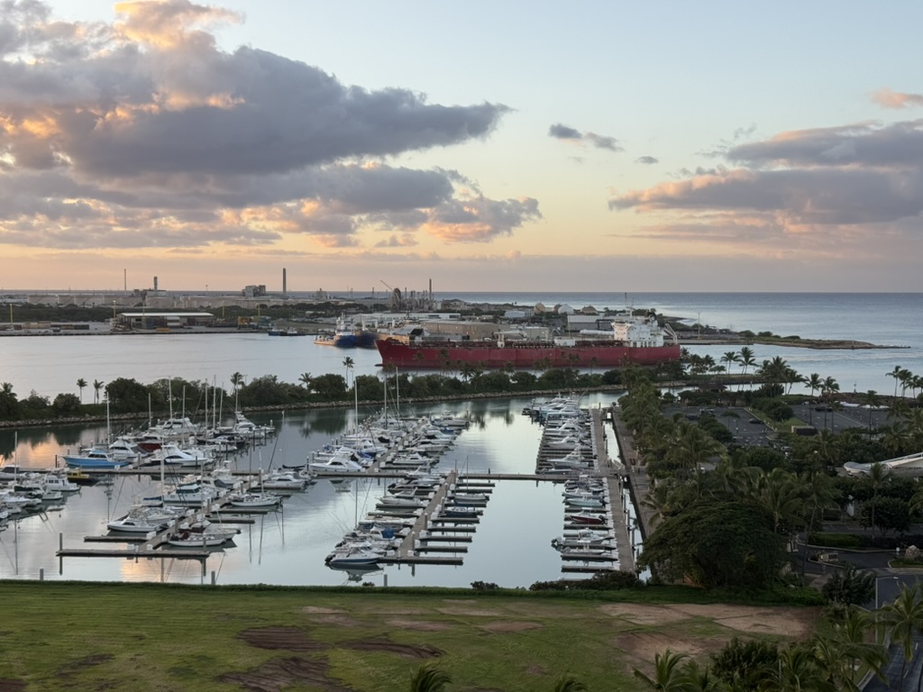 Marina at dawn with a red-hulled tanker moored beyond the boats