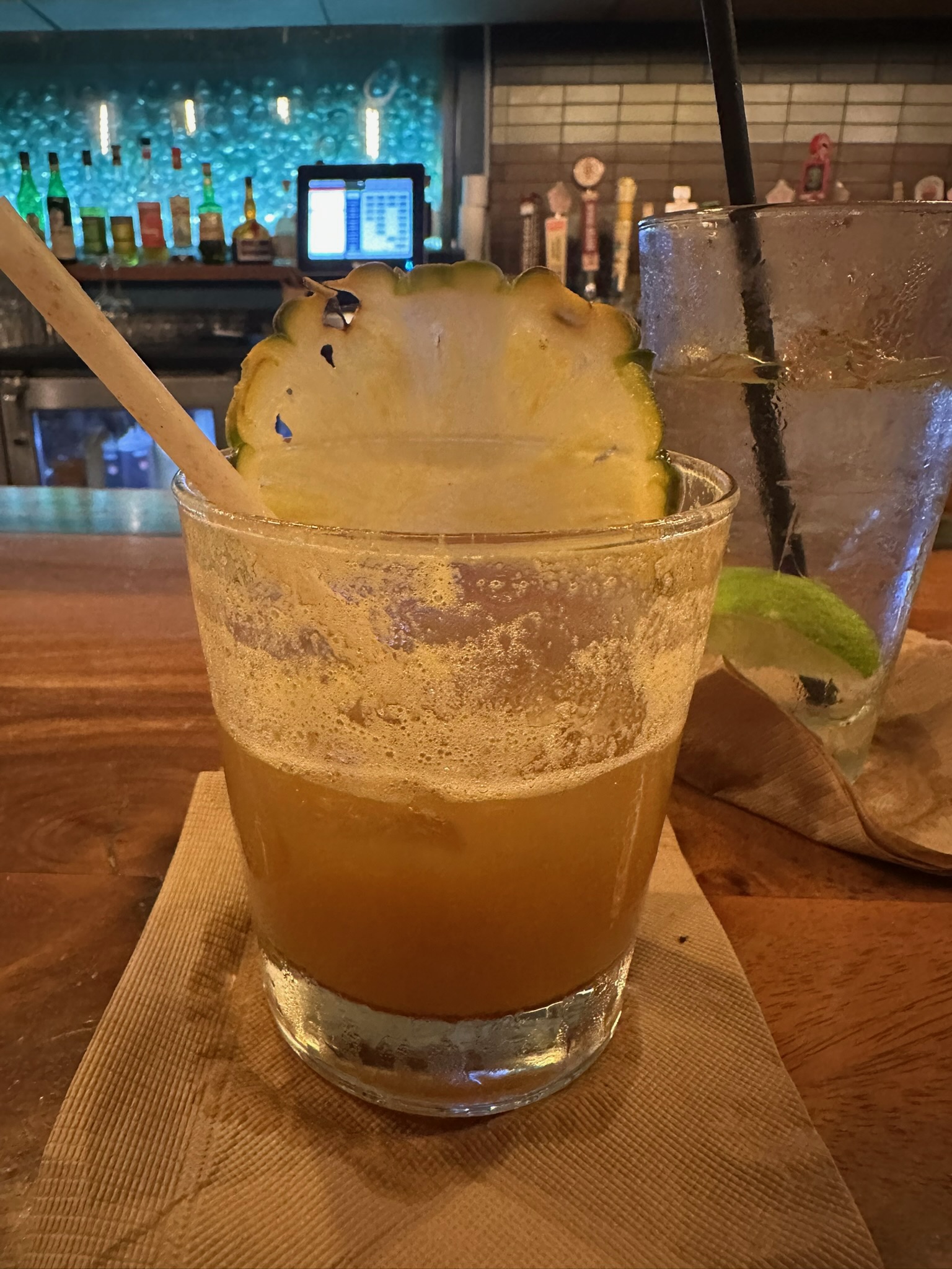A half-finished Monkeypod Kitchen Mai Tai with a pineapple-wheel garnish on the bar