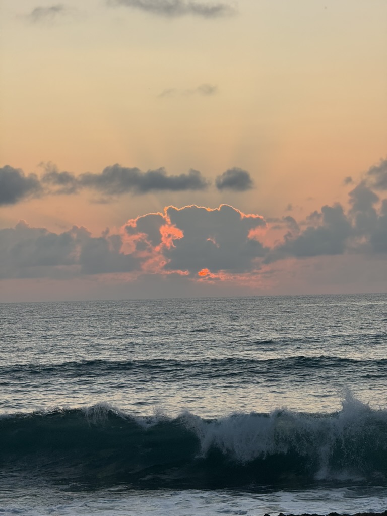 A wave breaking under a sun-orange cloud at the horizon