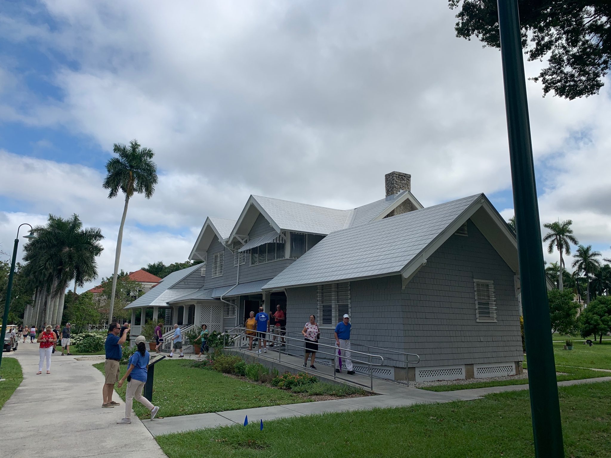 A gray Craftsman-style winter estate house with a wraparound porch, visitors gathered out front