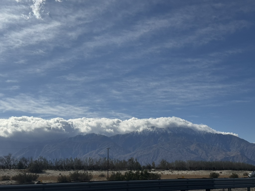 Snow-capped San Jacinto from the highway, cars in the foreground, a cloud bank capping the peaks