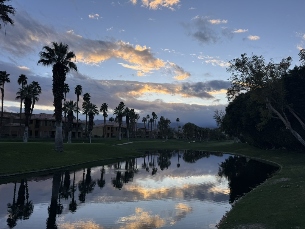 Golden sunset reflected in a resort lagoon, palms framing the horizon