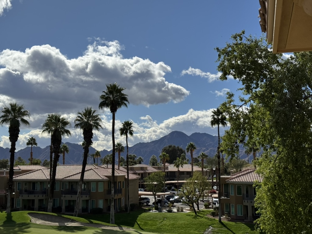 Villa exteriors viewed from a balcony — palms, tile roofs, mountains in the haze