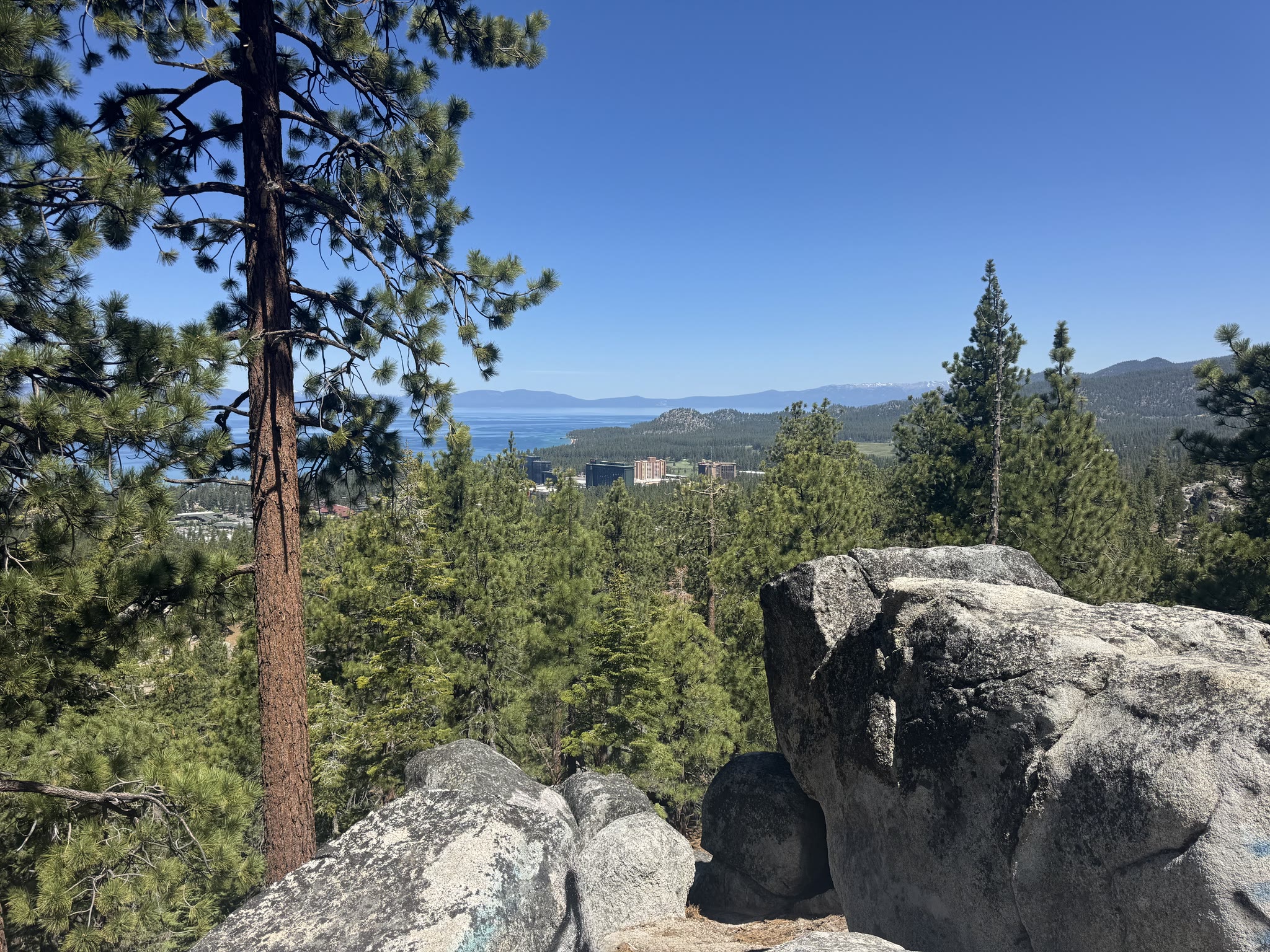 Tahoe seen from the trail — boulder outcrop in the foreground, the lake's south shore and the buildings at the state line beyond